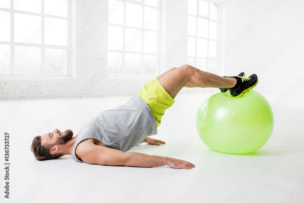 Handsome man exercising with fitball in the white gym interior