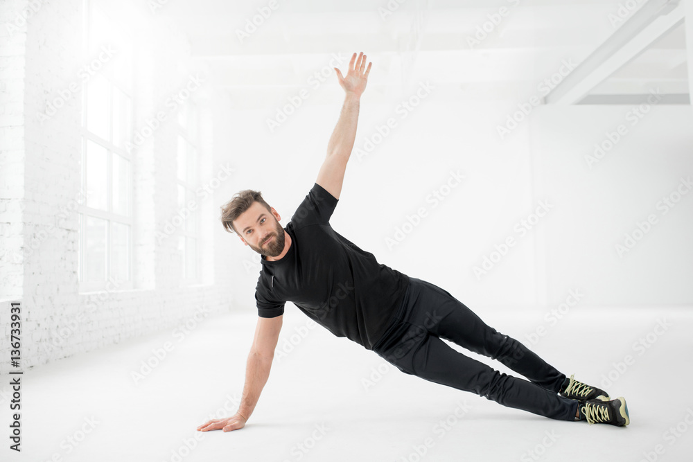 Handsome man in the black sportswear holding plank on the floor in the white gym interior