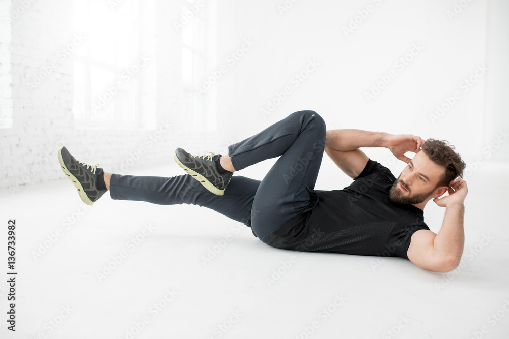 Handsome man in the black sportswear doing abs on the floor in the white gym interior