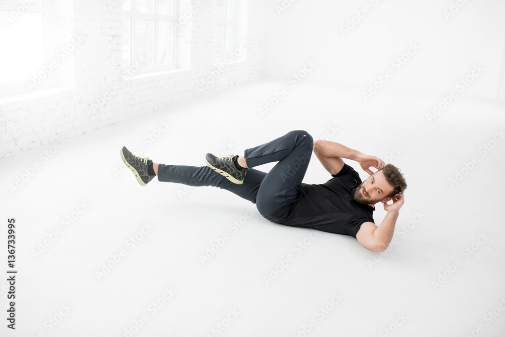 Handsome man in the black sportswear doing abs on the floor in the white gym interior