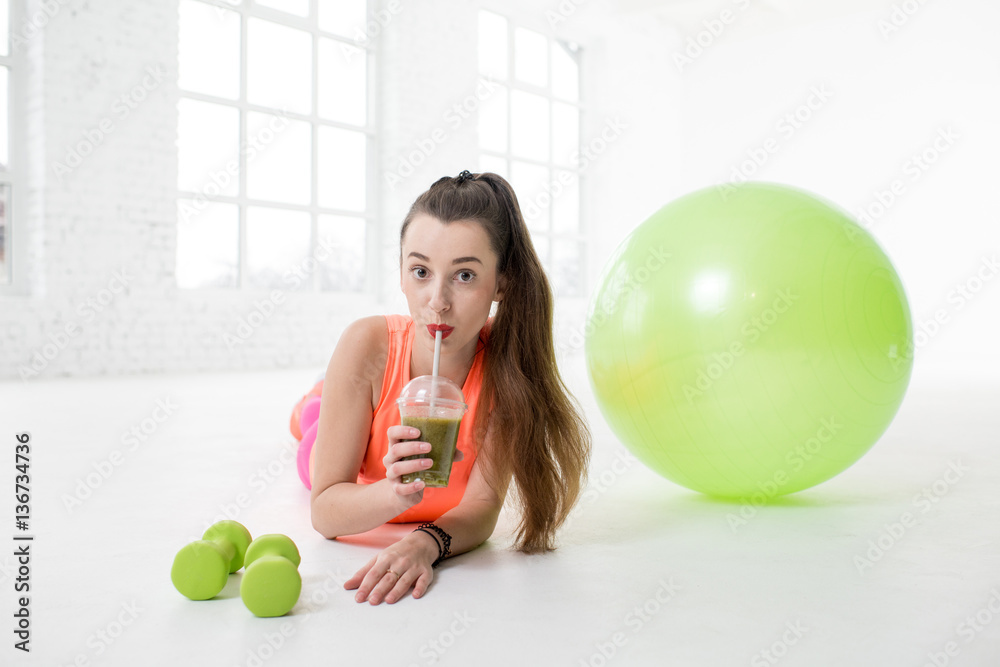 Portrait of young sport woman drinking kiwi fresh with dumbbells and fitness ball on the floor in th