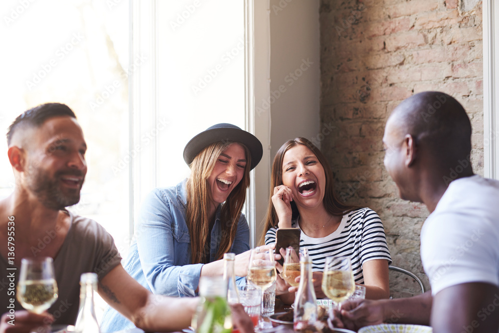 Friends laughing at something on phone at dinner