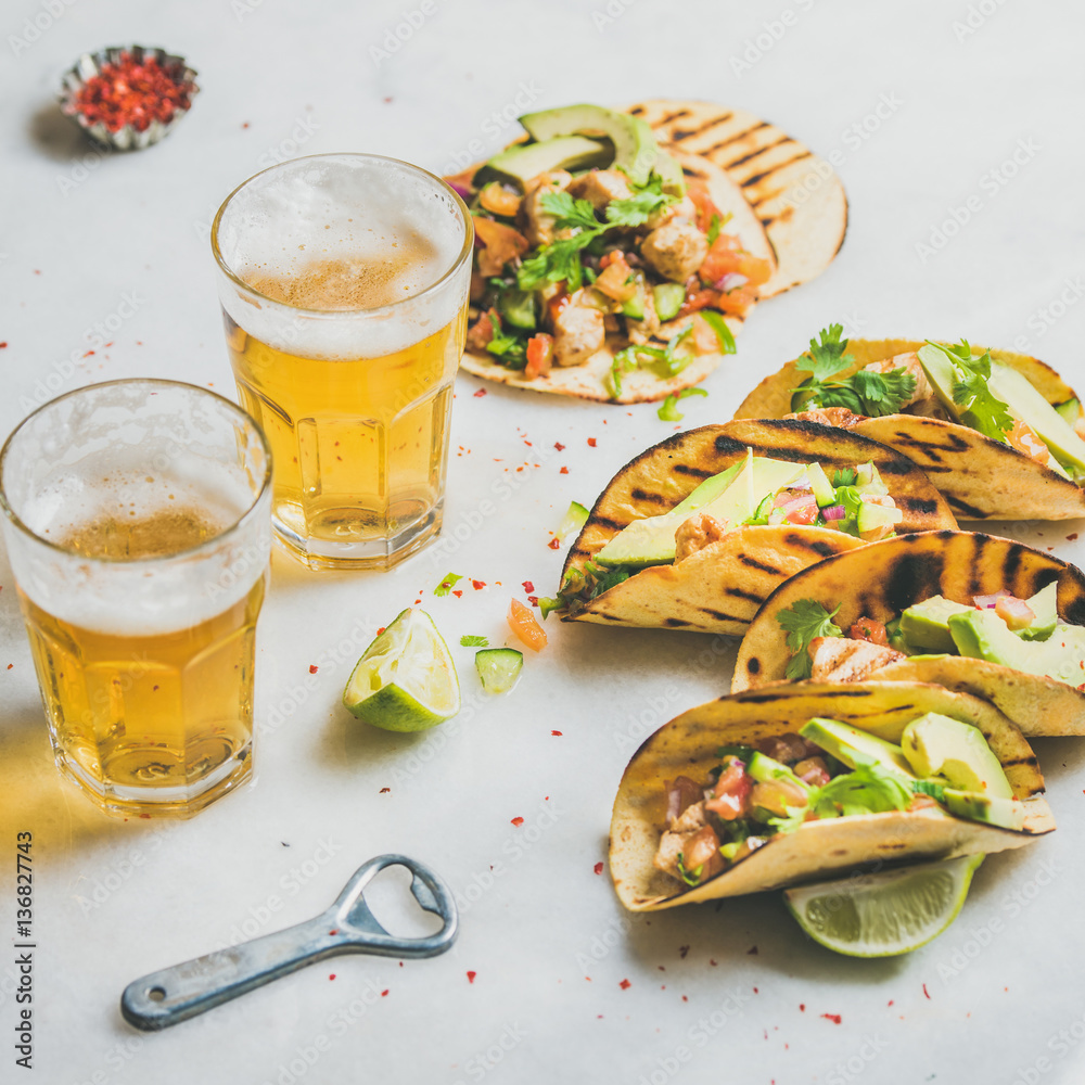 Healthy corn tortillas with grilled chicken fillet, avocado, fresh salsa, limes, beer in glasses ove