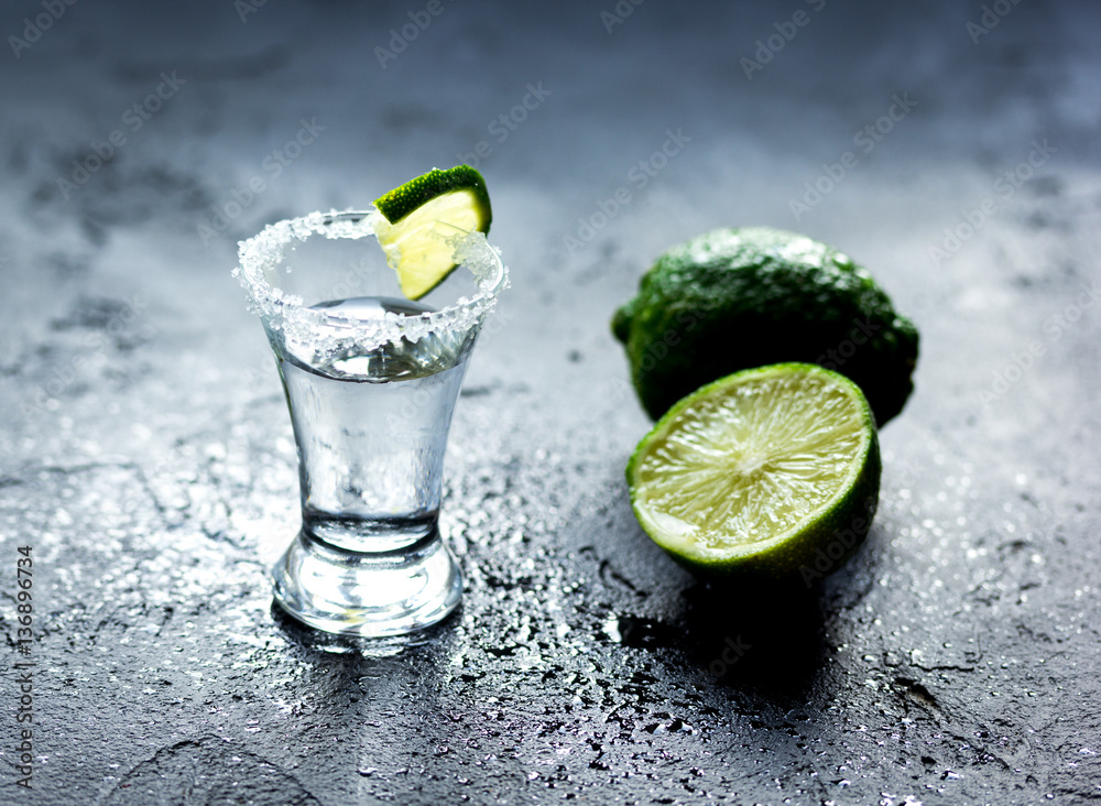 Tequila shot with lime slices and salt on dark background