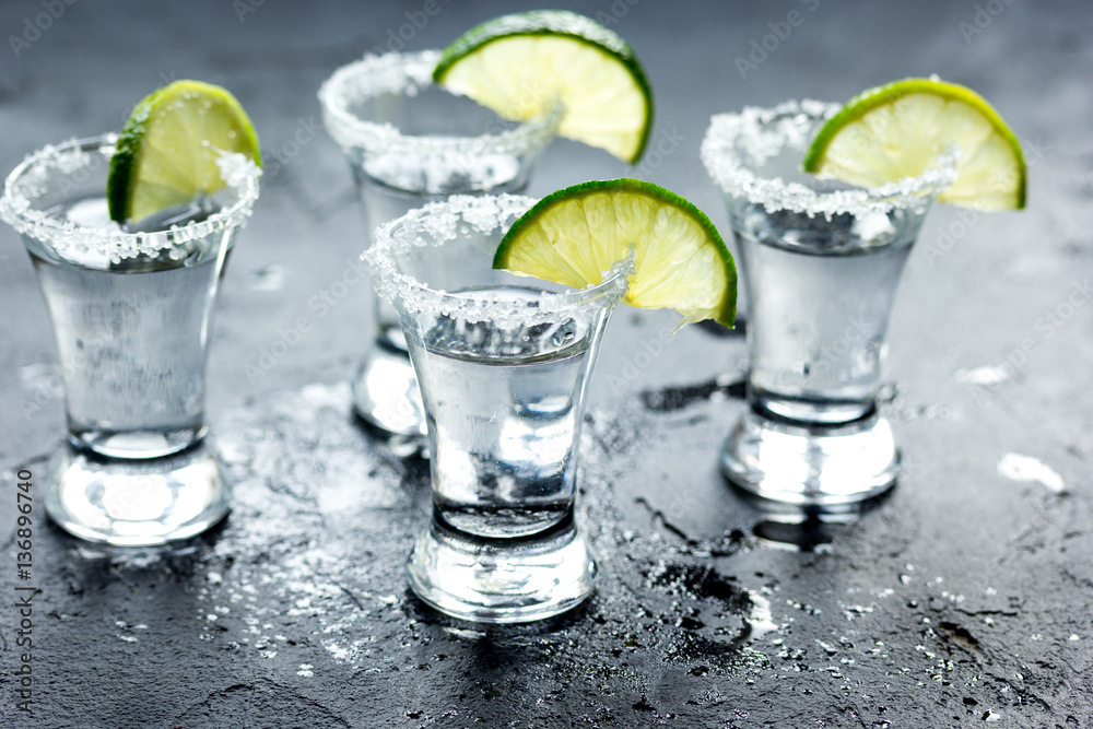 Tequila shot with lime slices and salt on dark background