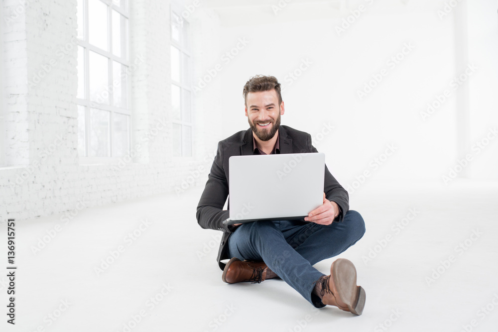 Elegant businessman working with laptop on the floor at the big white office interior