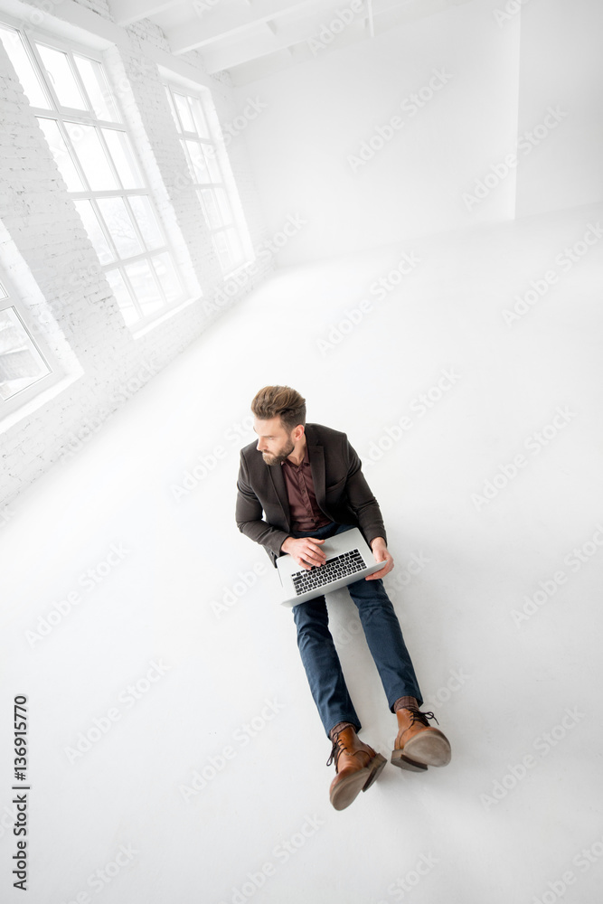 Elegant businessman working with laptop on the floor at the big white office interior