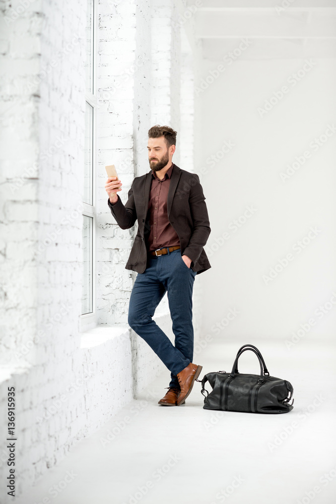 Elegant businessman standing with phone near the window in the white office interior