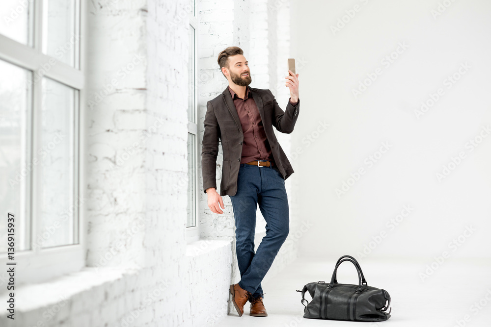 Elegant businessman standing with phone near the window in the white office interior