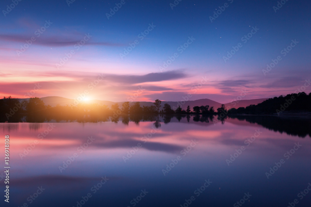 Mountain lake with moonrise at night. Night landscape with river, trees, hills, moon and colorful pu