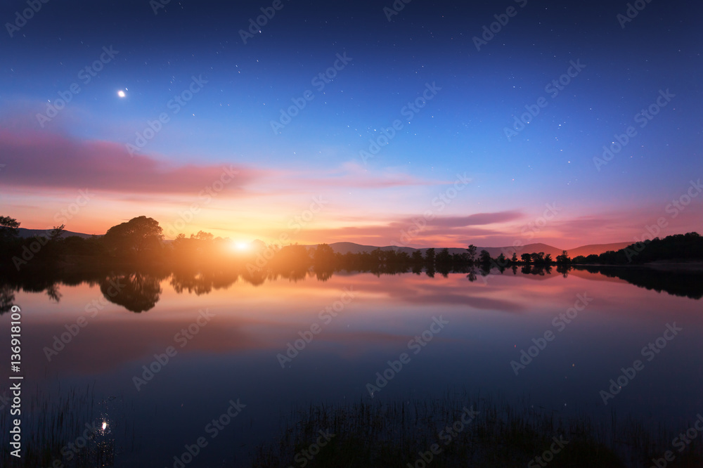 Mountain lake with moonrise at night. Night landscape with river, trees, hills, moon, stars and colo