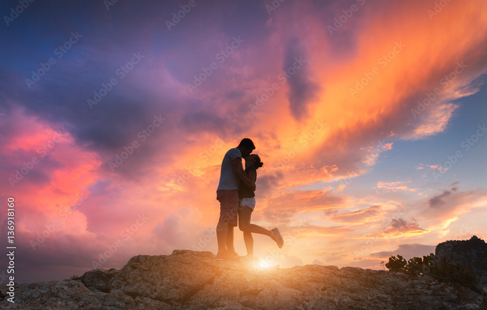 Silhouettes of a hugging and kissing man and girlfriend on the mountain peak at sunset. Man and woma