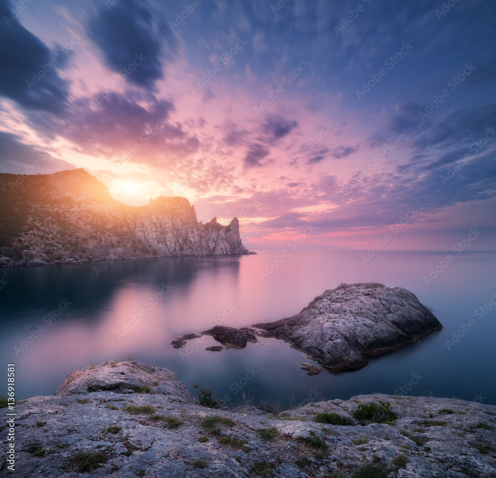 Rock in the sea against mountains and colorful cloudy sky at sunset. Landscape with mountains, sea, 