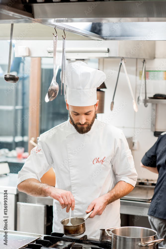 Handsome chef cook in uniform cooking food on the gas stove at the restaurant kitchen