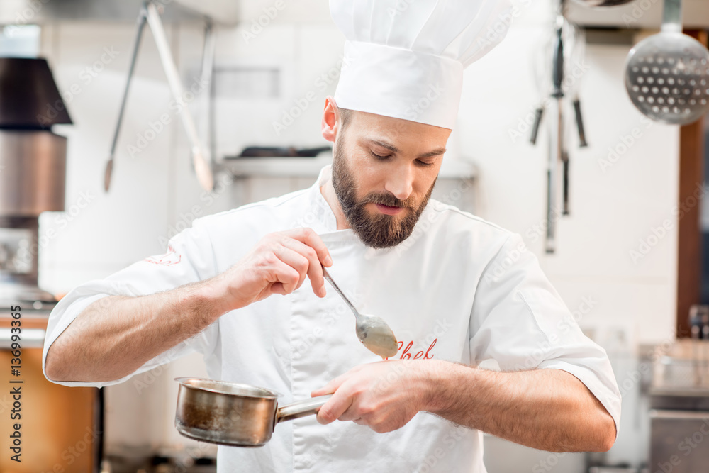 Handsome chef cook in uniform tasting sause at the kitchen