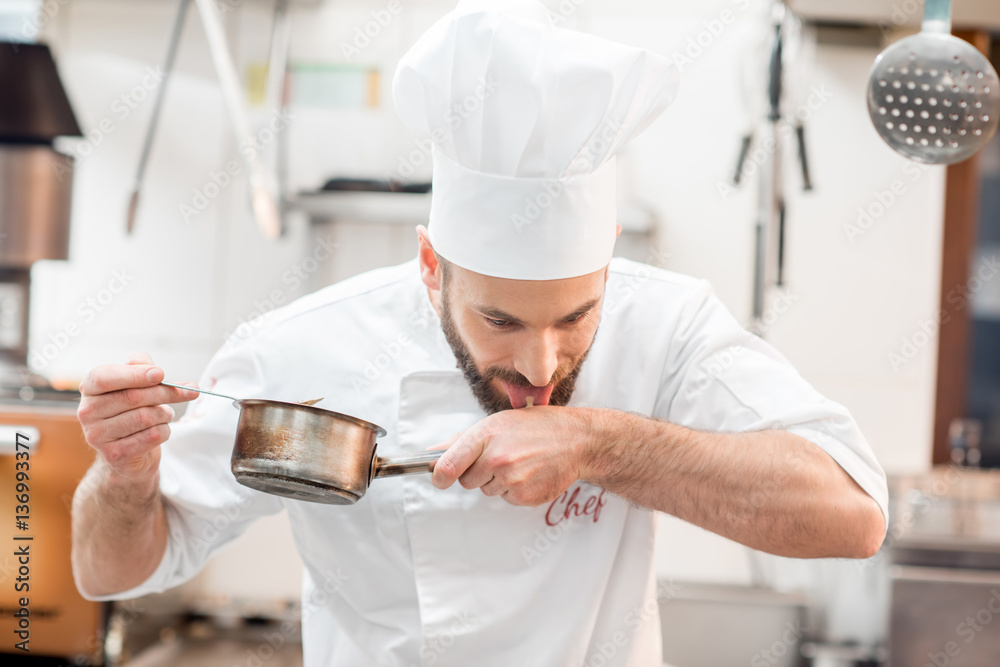 Handsome chef cook in uniform tasting sause at the kitchen