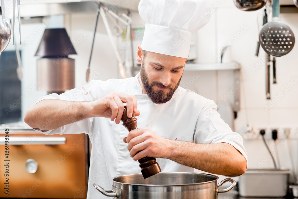 Chef cook in uniform peppering soup in the big cooker at the restaurant kitchen