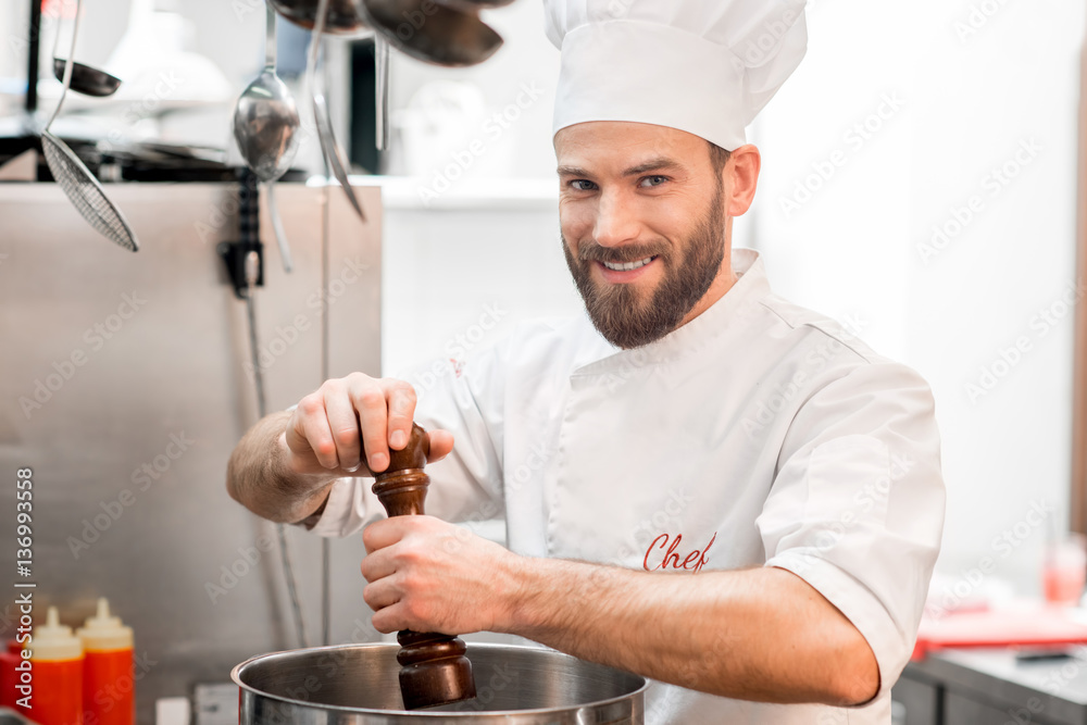 Chef cook in uniform peppering soup in the big cooker at the restaurant kitchen