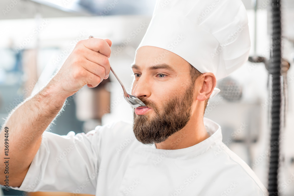 Handsome chef cook tasting with spoon food at the beautiful restaurant kitchen