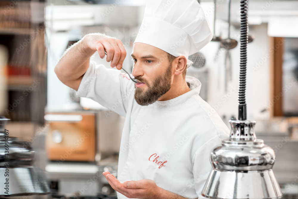 Handsome chef cook tasting with spoon food at the beautiful restaurant kitchen