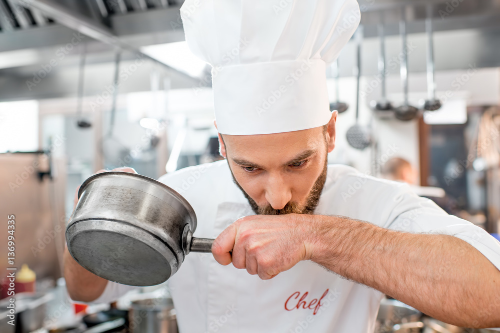 Handsome chef cook in uniform tasting sause at the kitchen