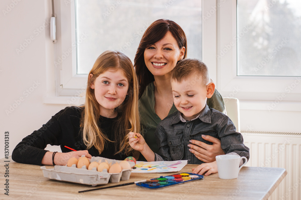 A mother and her kids painting Easter eggs. Happy family preparing eggs for Easter