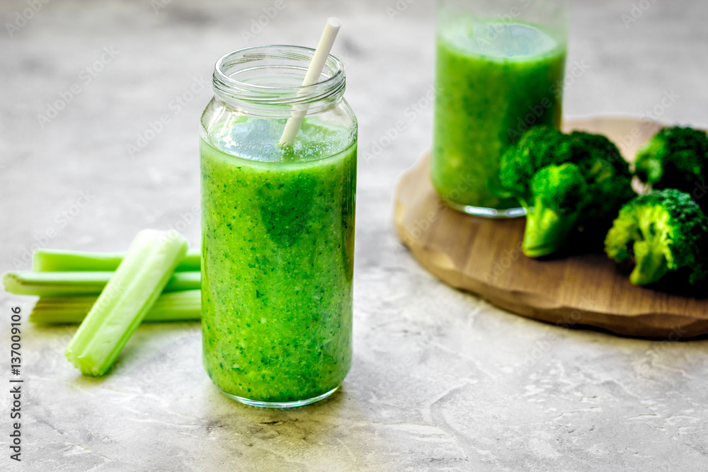 Green vegetable smoothie in glass at gray background