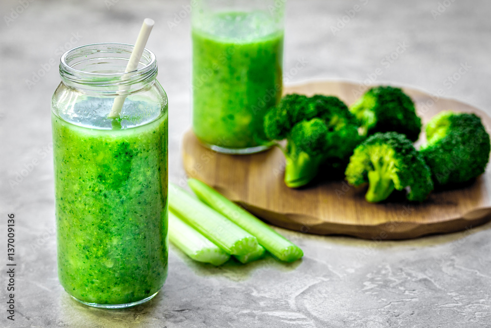 Green vegetable smoothie in glass at gray background