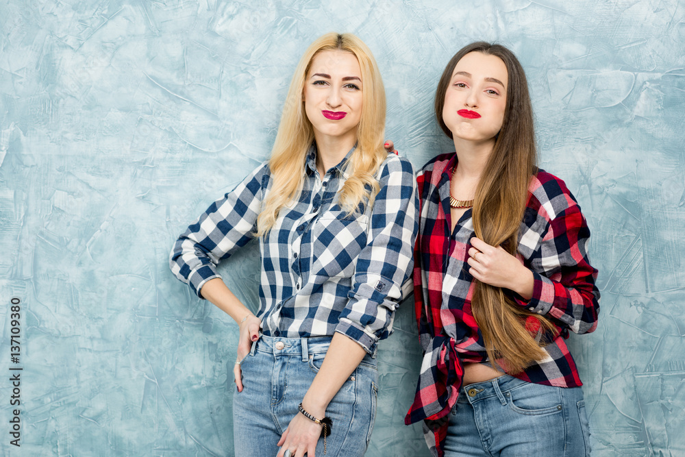 Portrait of two female friends in checkered shirts and jeans having fun together on the blue painted