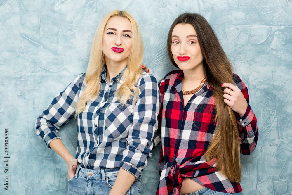 Portrait of two female friends in checkered shirts and jeans having fun together on the blue painted