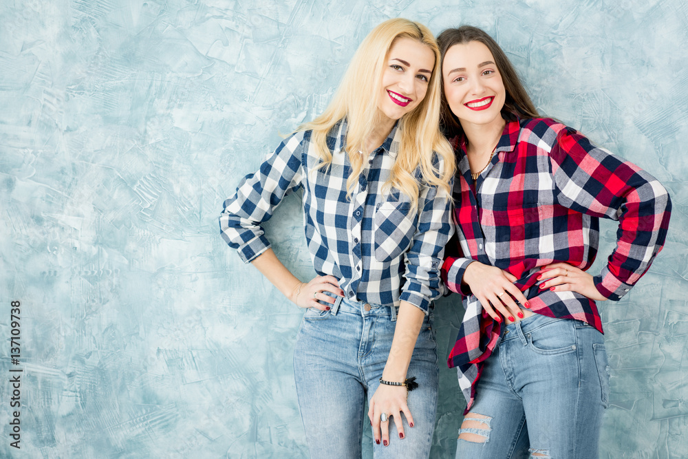 Portrait of two female friends in checkered shirts and jeans having fun together on the blue painted