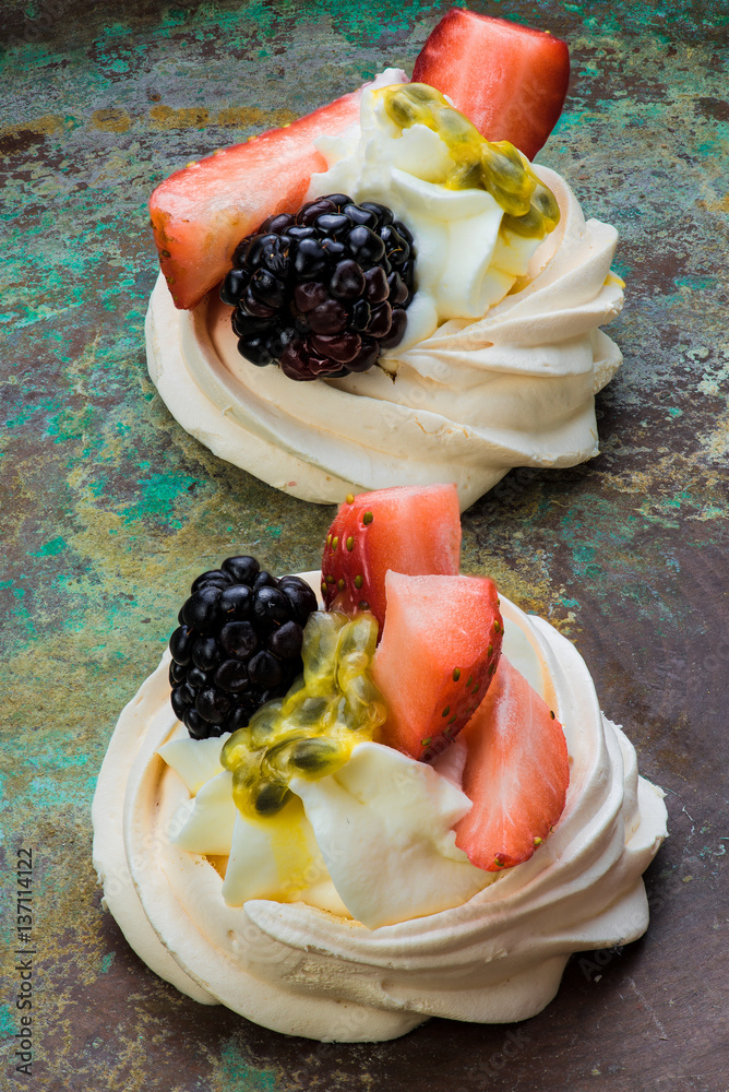 Mini Pavlova meringue cakes with berries and passion fruits on rustic vintage background. Top view.