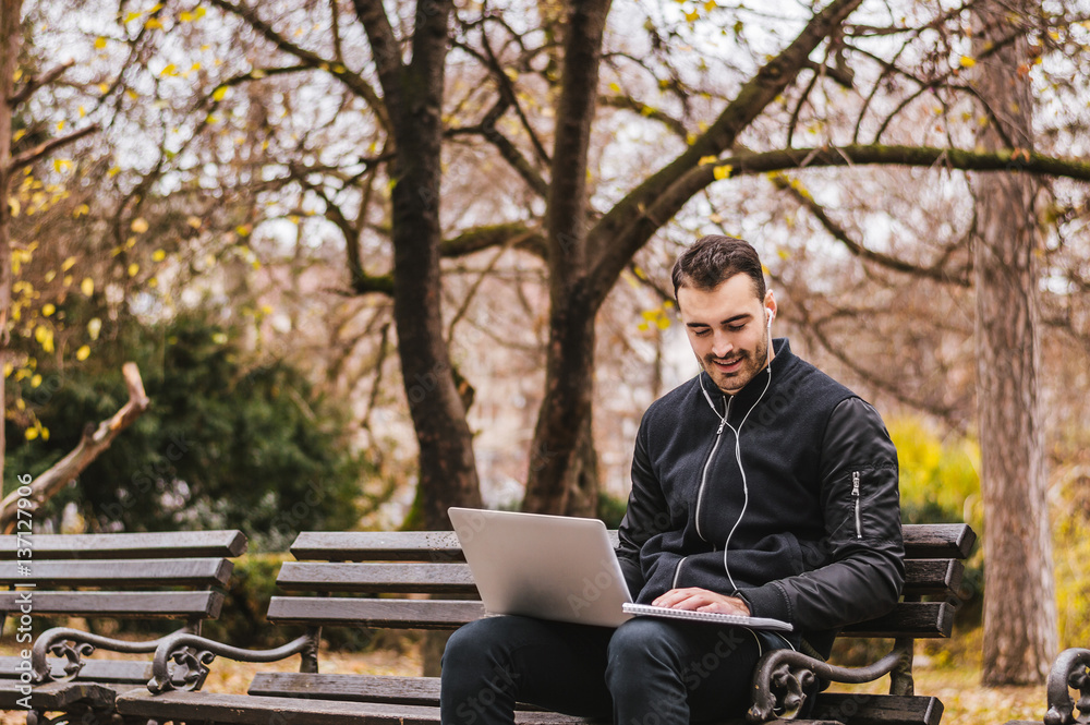 Young businessman sitting on bench with laptop on his lap