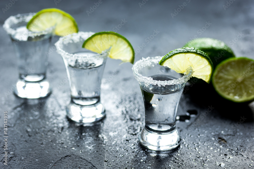 Tequila shot with lime slices and salt on dark background