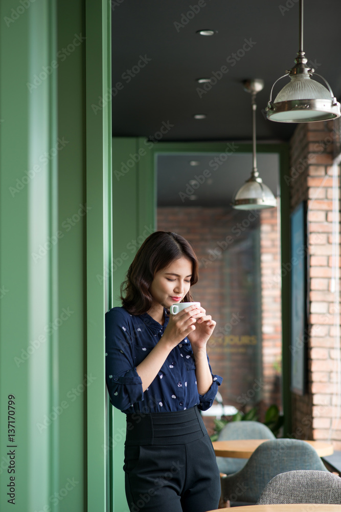 Portrait of happy young business woman with mug in hands drinking coffee in the morning at restauran