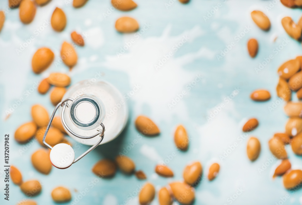 Dairy alternative milk. Almond milk in bottle and fresh nuts over blue background, top view, selecti