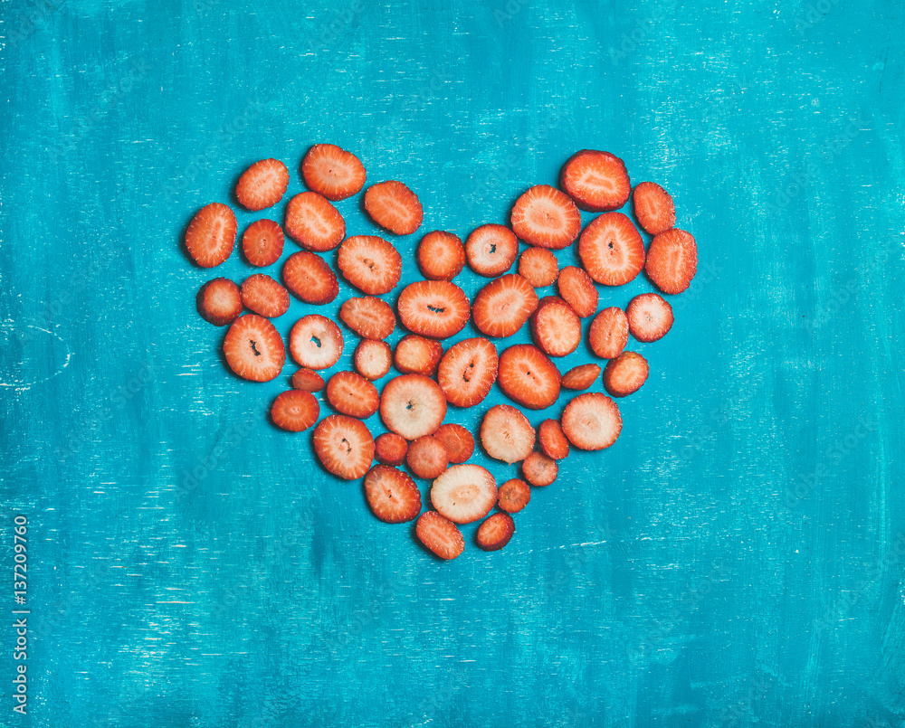 Pieces of fresh red strawberry placed in shape of heart over bright blue painted wooden background, 