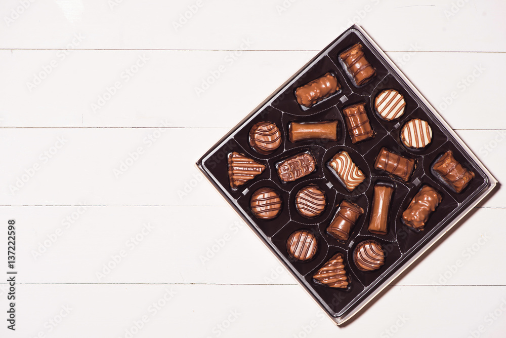 top view of various chocolate pralines in box on white wooden background.