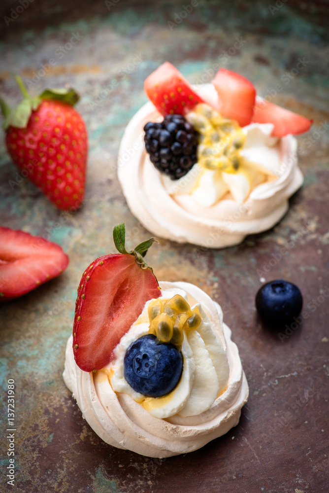 Mini Pavlova meringue cakes with berries and passion fruits on rustic vintage background. Top view.