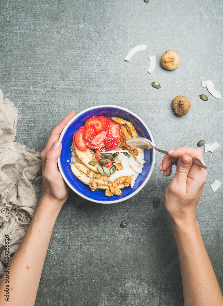 Yogurt, granola, seeds, fresh and dry fruits and honey in blue ceramic bowl in woman s hands over g