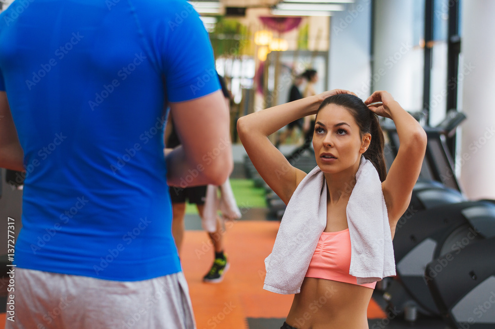 Young male personal trainer talking with young fitness woman while she having a break