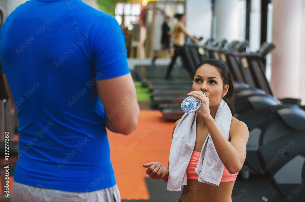 Young male personal trainer talking with young fitness woman while she having a break