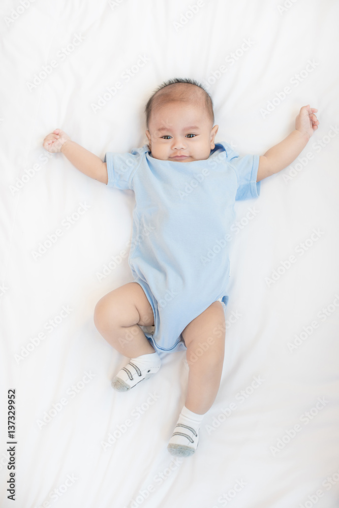 Portrait of 4 month Asian baby lying on white bed in bedroom at house, top view.