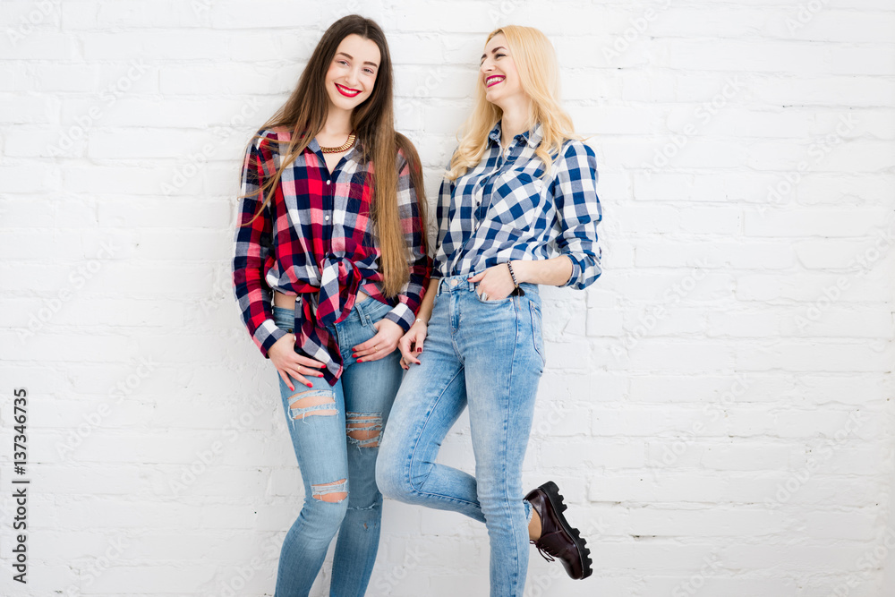 Female friends in checkered shirts and jeans standing together on the white wall background