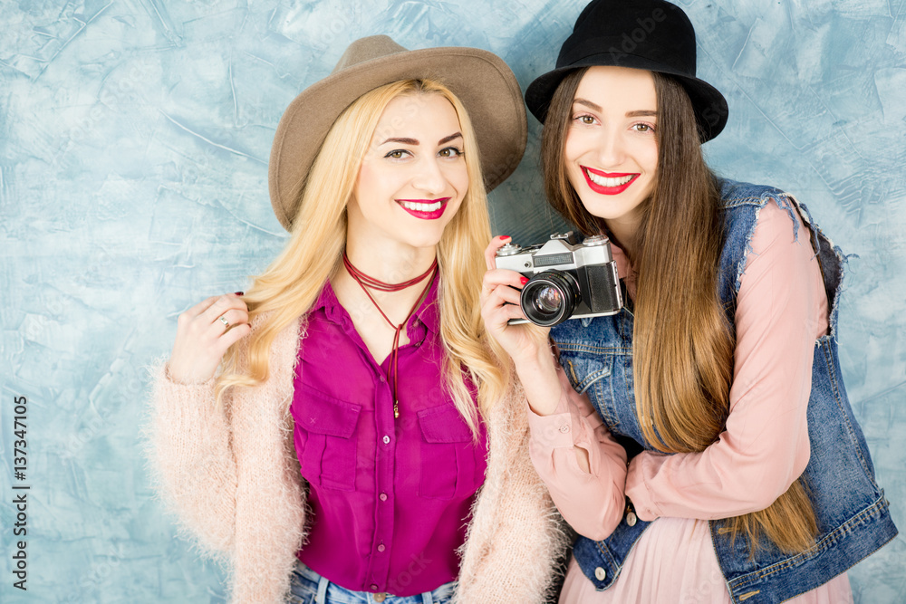 Female stylish friends having fun with photo camera on the blue wall background