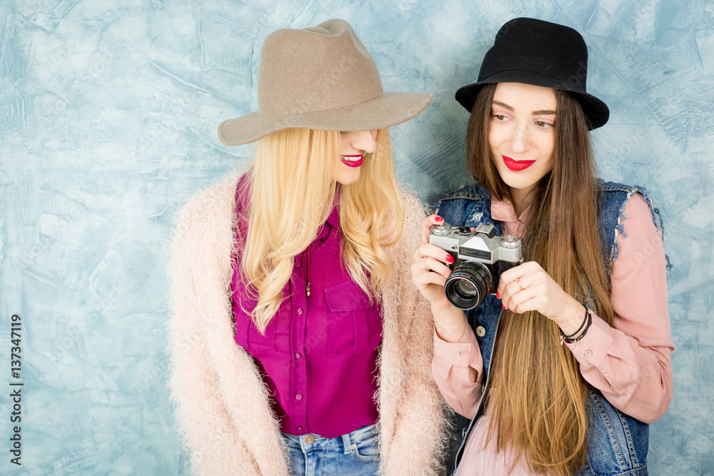 Female stylish friends having fun with photo camera on the blue wall background