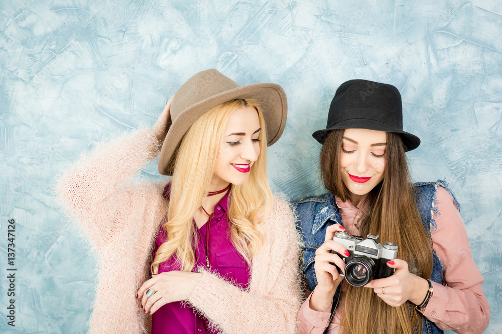 Female stylish friends having fun with photo camera on the blue wall background