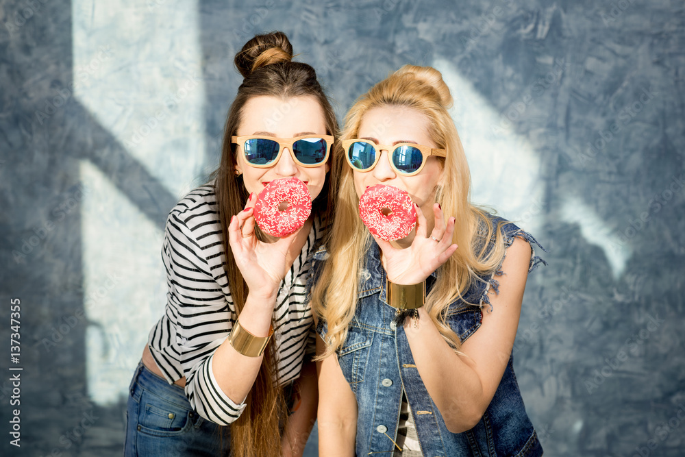 Playful women having fun with sweet donuts on the blue wall background