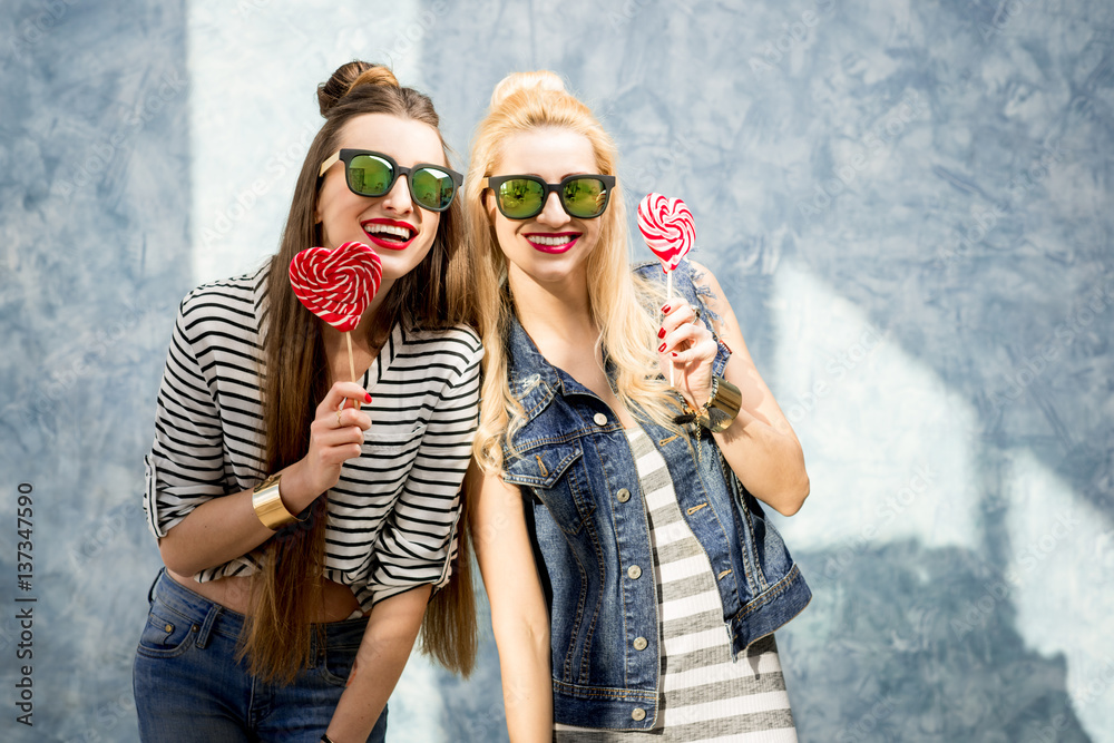 Young female friends having fun with candies standing on the blue wall background