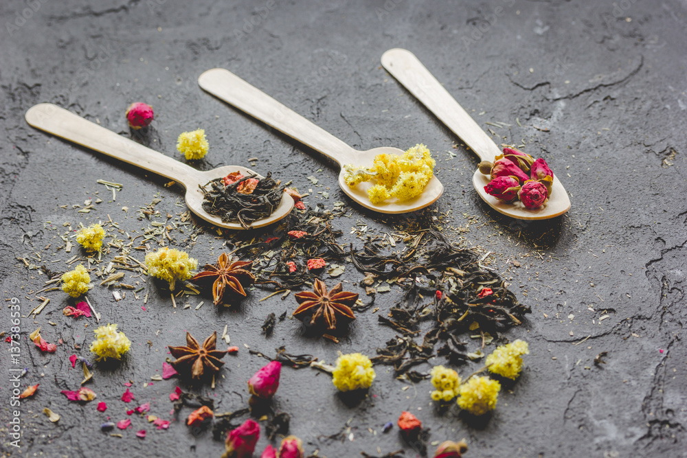 Spoons with herbs on dark stone background